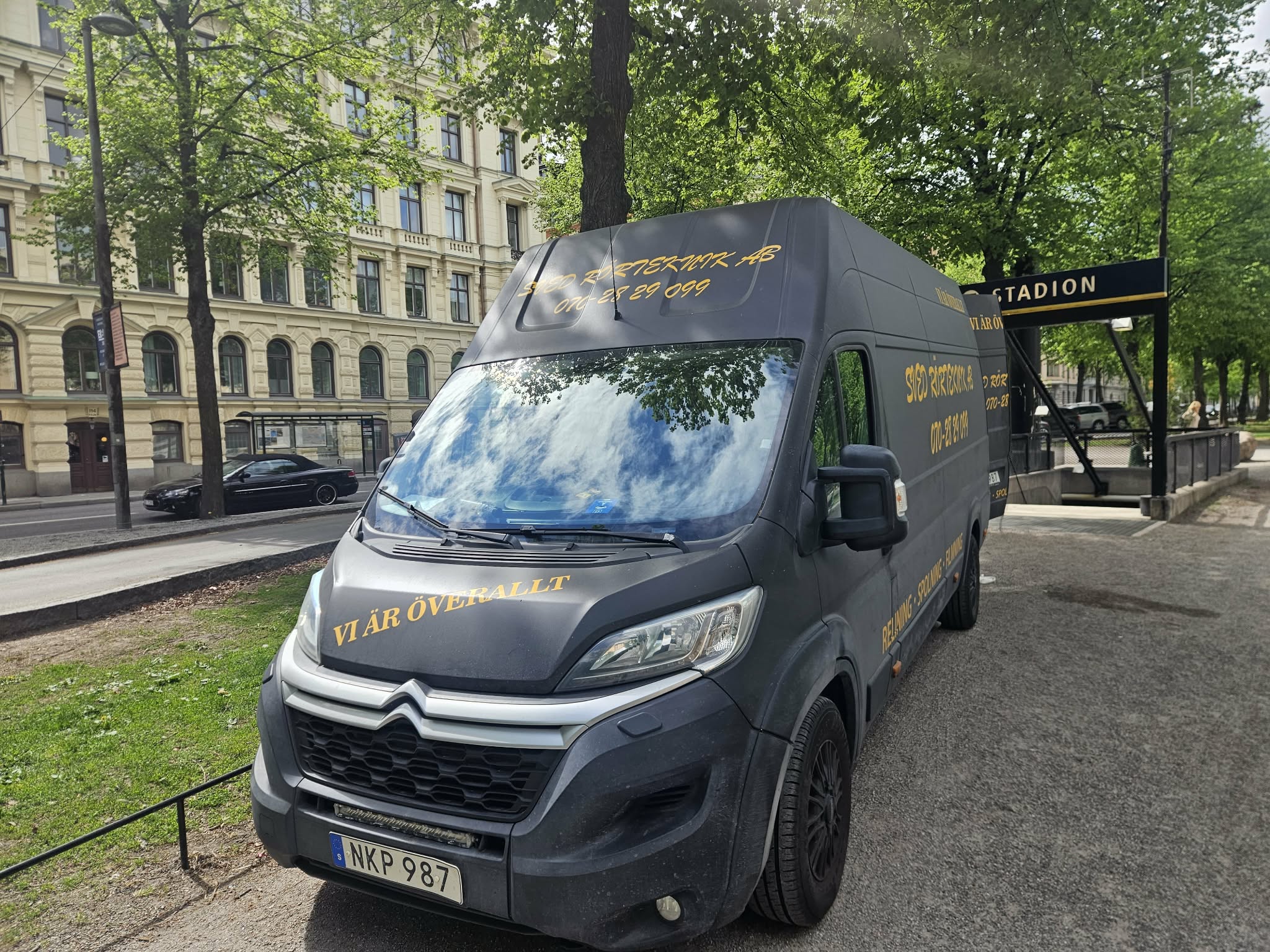 Servicebilen parkerad på en trädkantad gata i stadsmiljö, sedd framifrån.